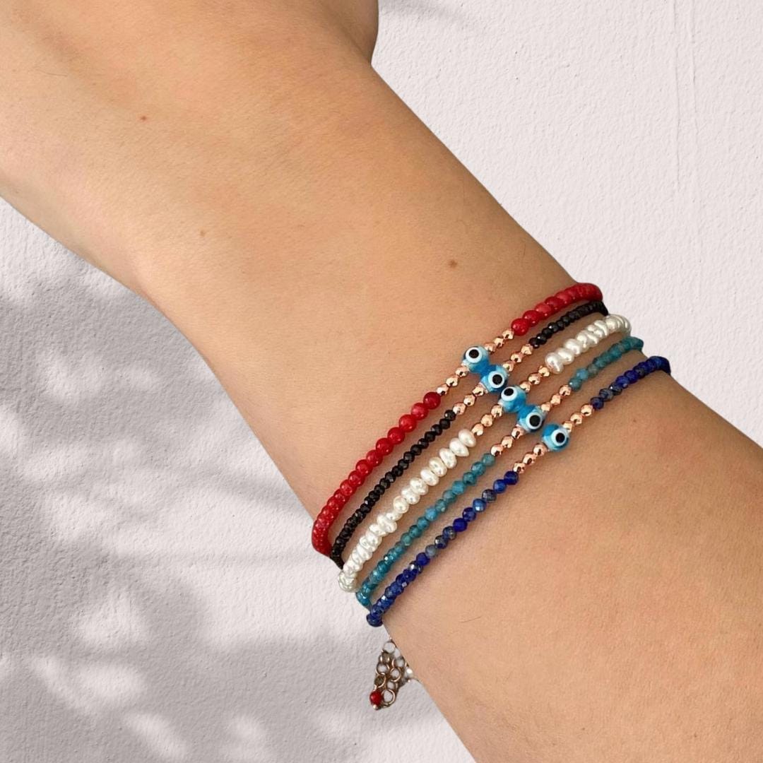 Stacked Apatite gemstone bracelets with mini evil eye charms in vibrant colours shown on a wrist for stylish appeal.
