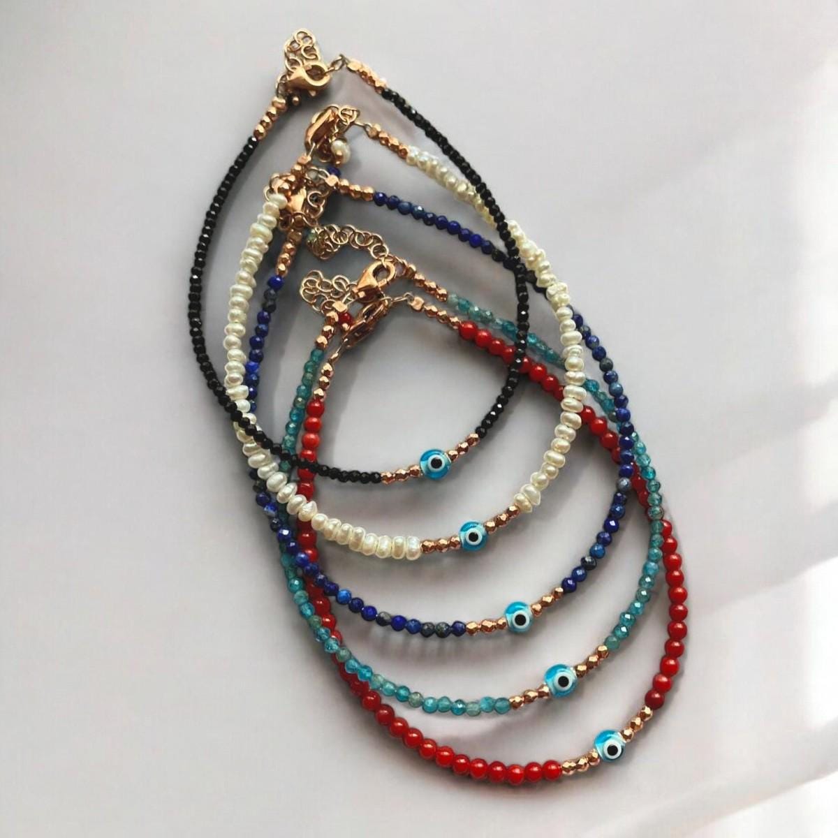 A display of colourful Apatite gemstone bracelets featuring mini evil eye charms, elegantly arranged on a light background.