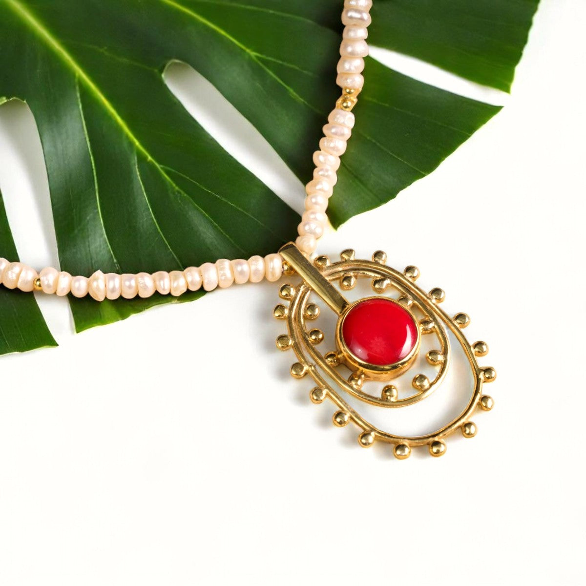 Fairy Tale necklace featuring pearls and coral gemstone, displayed elegantly against a green leaf background.