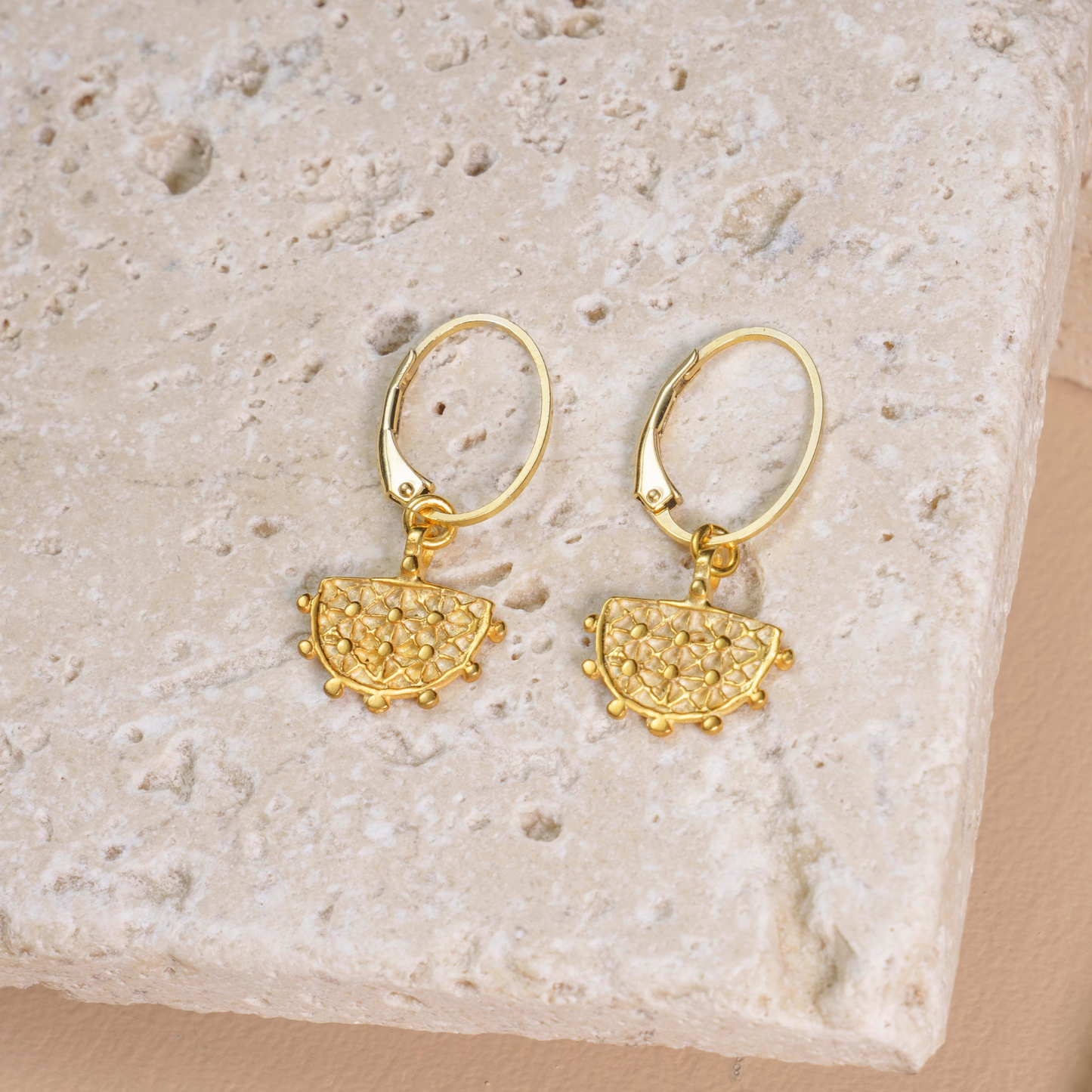 Gold-plated silver earrings inspired by Hittite Sun symbols, elegantly placed on a textured stone backdrop.