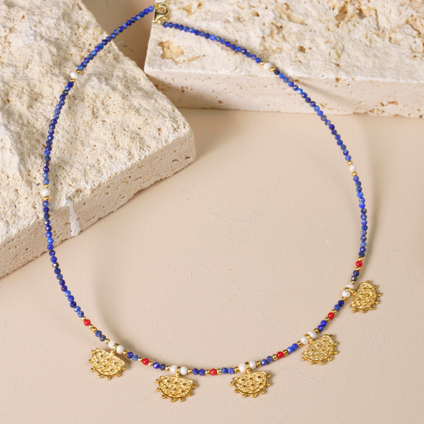Elegant Hittite Sun Symbol necklace with vibrant lapis lazuli and gold adornments, displayed on neutral textured background.
