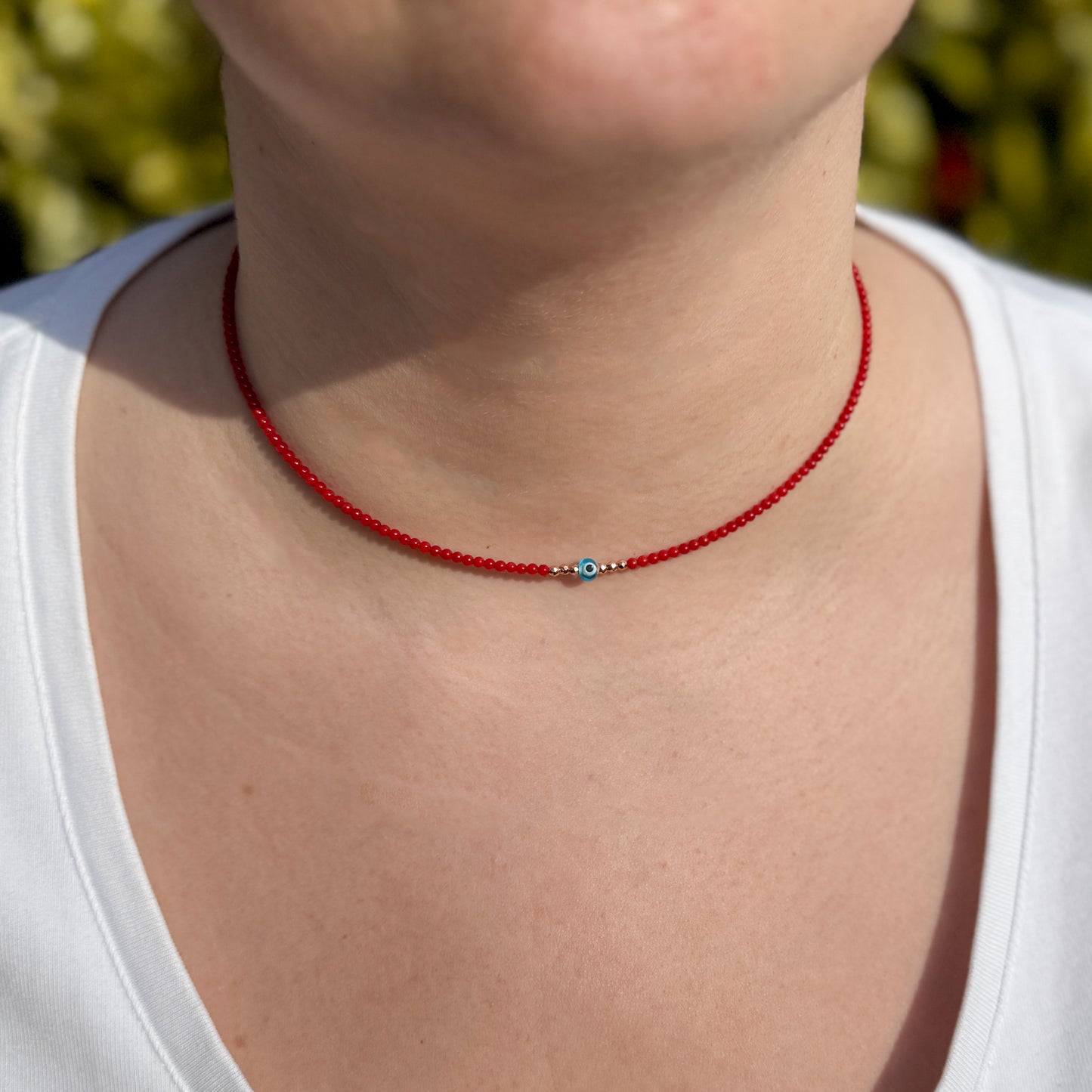 Mini Evil Eye Coral Gemstone Necklace on a neck, featuring vibrant red beads and a central blue evil eye charm.