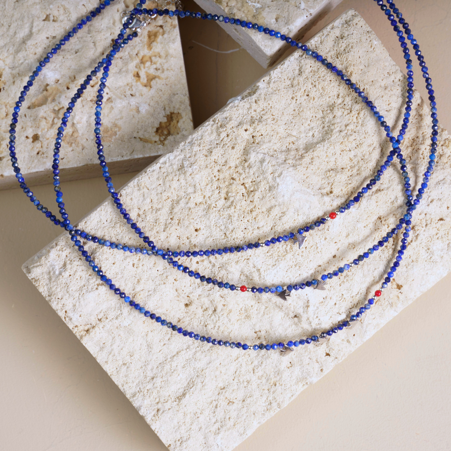 Minimal lapis lazuli necklace with silver bird pendants, set against a textured stone backdrop for a trendy jewellery display.