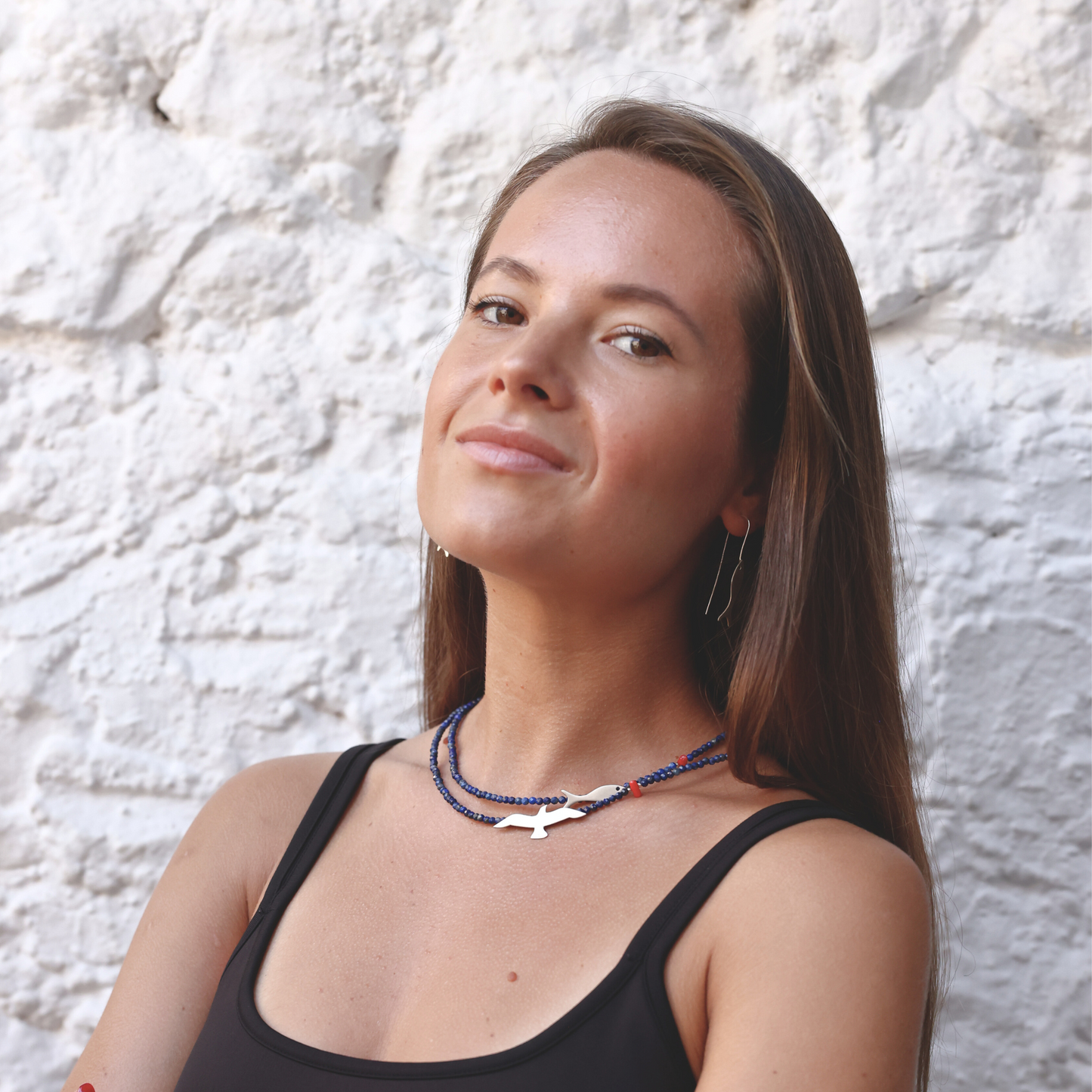 Model wearing a Seagull & Fish necklace made of lapis and silver, paired with a casual outfit, set against a textured wall.