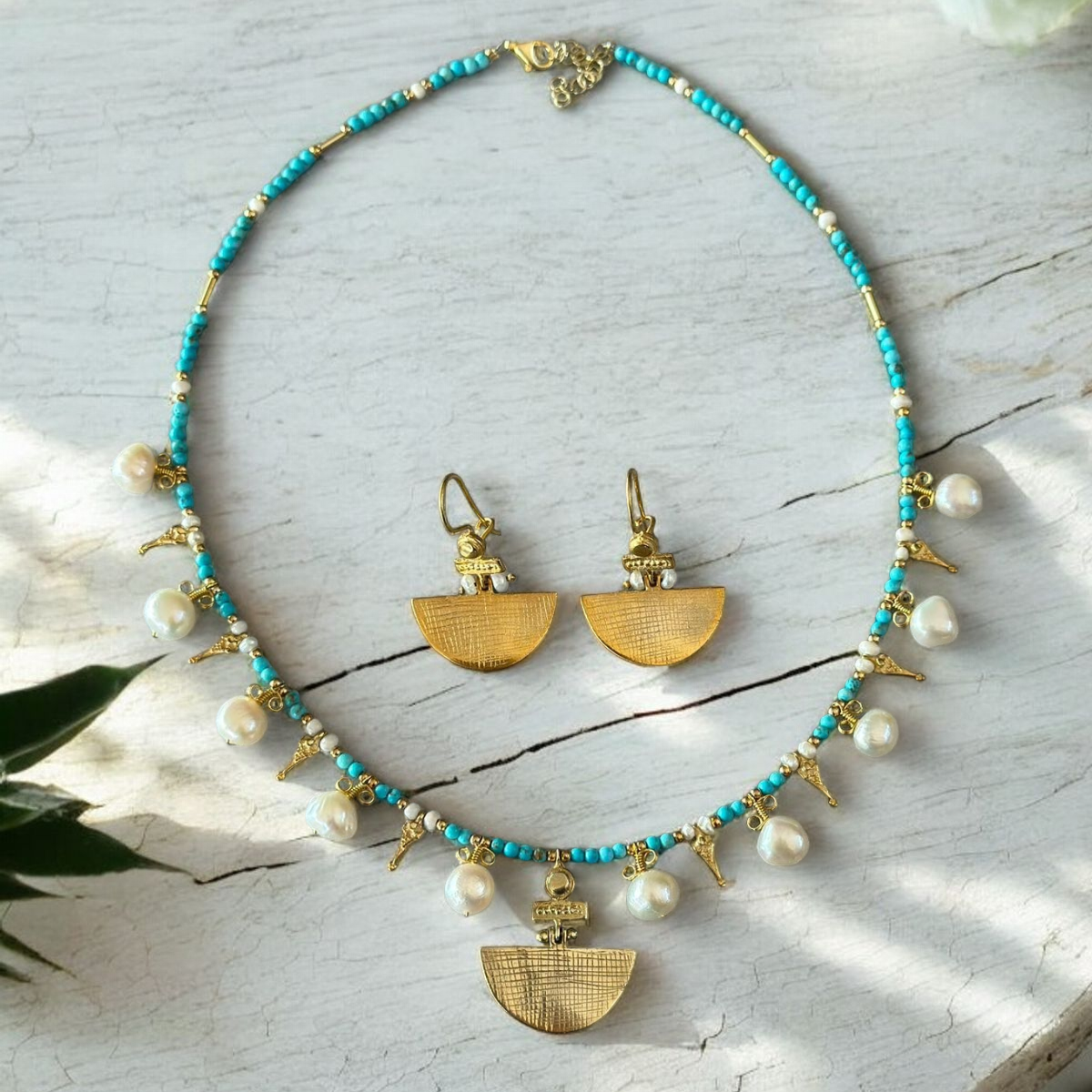 Selena Turquoise Necklace and Earrings Set - 14K Gold Plated with intricate gold accents and pearl detailing, displayed on a white rustic surface.