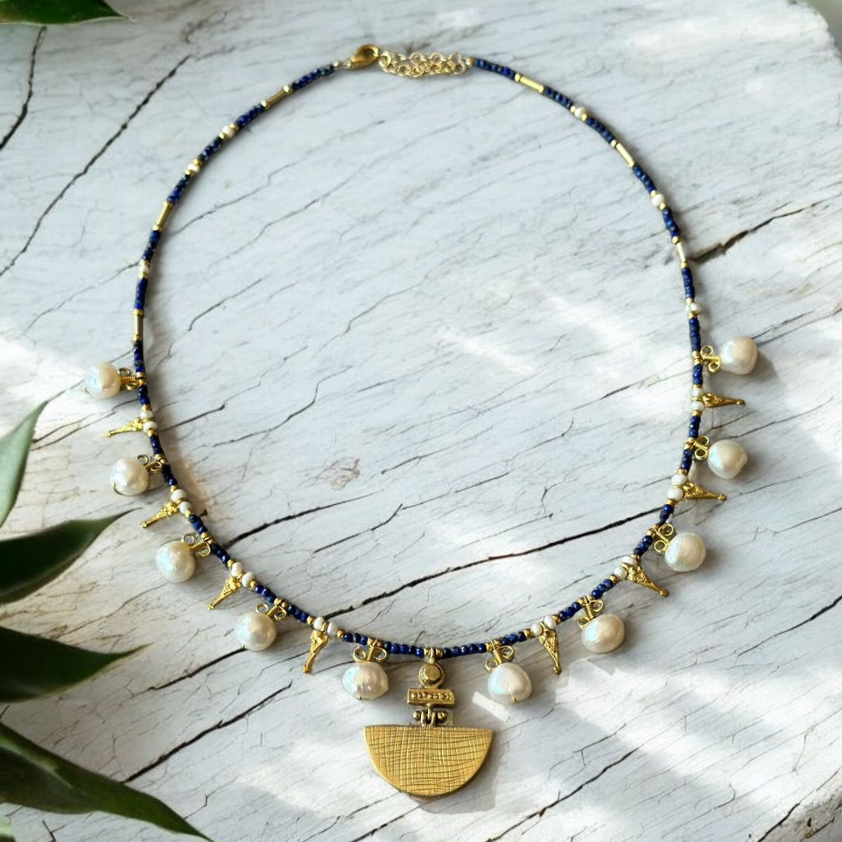 Selene Lapis Lazuli Gemstone and Pearl Necklace Gold Plated displayed on a white background with green plant accents
