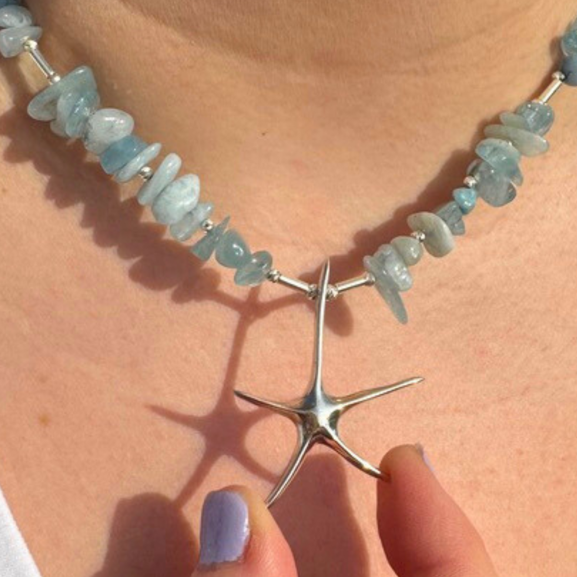 Close-up of a handmade aquamarine necklace showcasing a silver starfish pendant, emphasising artistic and nautical design.