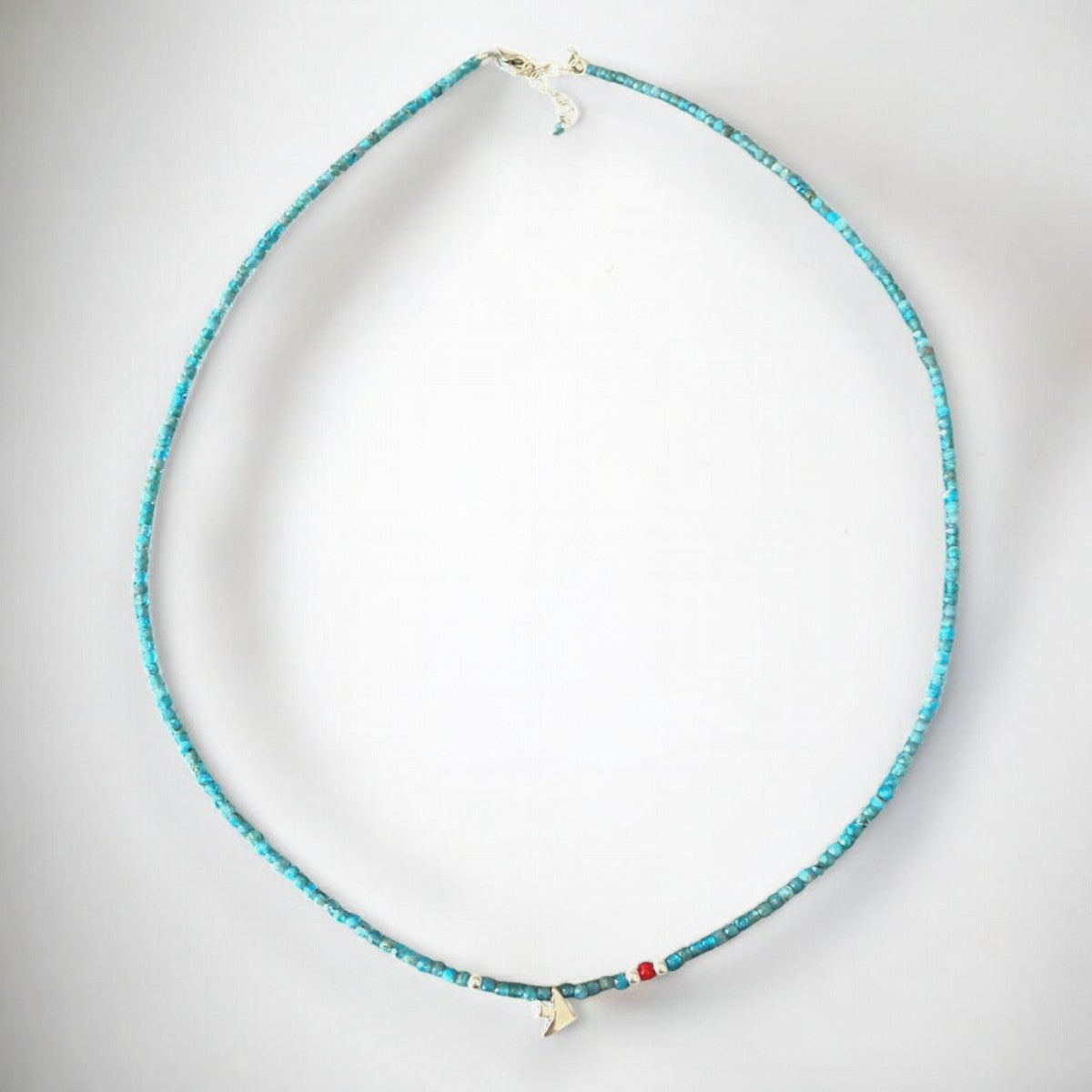 Elegant Birdie Minimal Silver Necklace adorned with a delicate turquoise beaded chain against a white background.