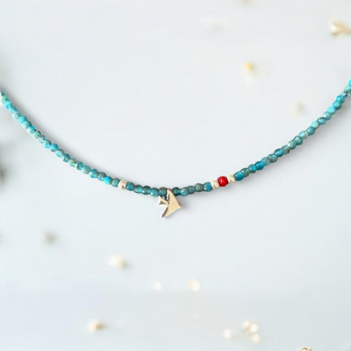 A minimal silver necklace with a bird charm and turquoise beads, perfect for an everyday chic look.