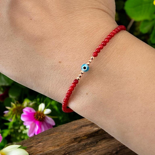 Coral gemstone bracelet featuring a mini evil eye charm, elegantly displayed on a wrist against a floral background.