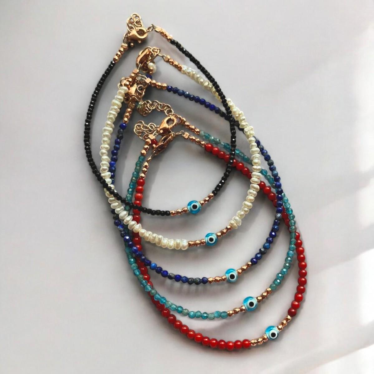 Assorted coral gemstone bracelets adorned with mini evil eye charms and golden accents, displayed on a white surface.