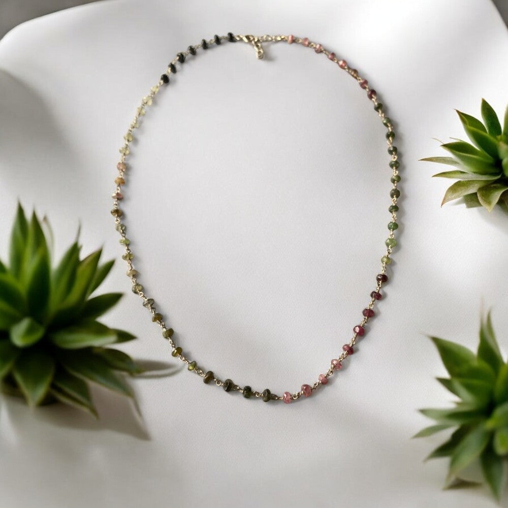 Dainty multicolour tourmaline gemstone chain necklace elegantly displayed alongside green succulent plants.