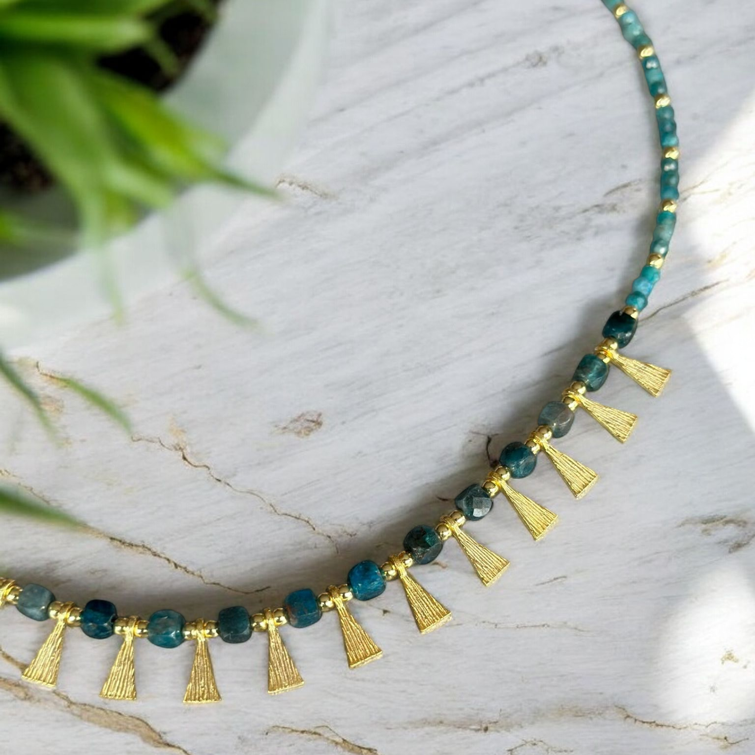 Eva Necklace with Apatite Gemstone in 925 Sterling Silver Gold Plated displayed on a marble background next to a green plant.
