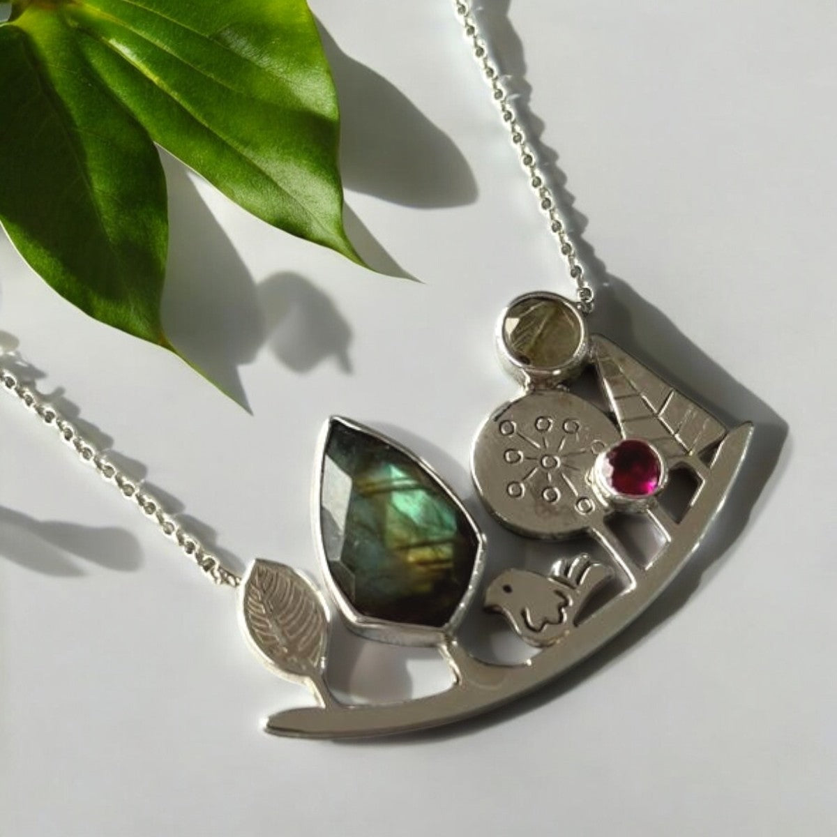 Landscape-themed silver necklace with intricate design, gemstones, and nature-inspired motifs captured in soft lighting.