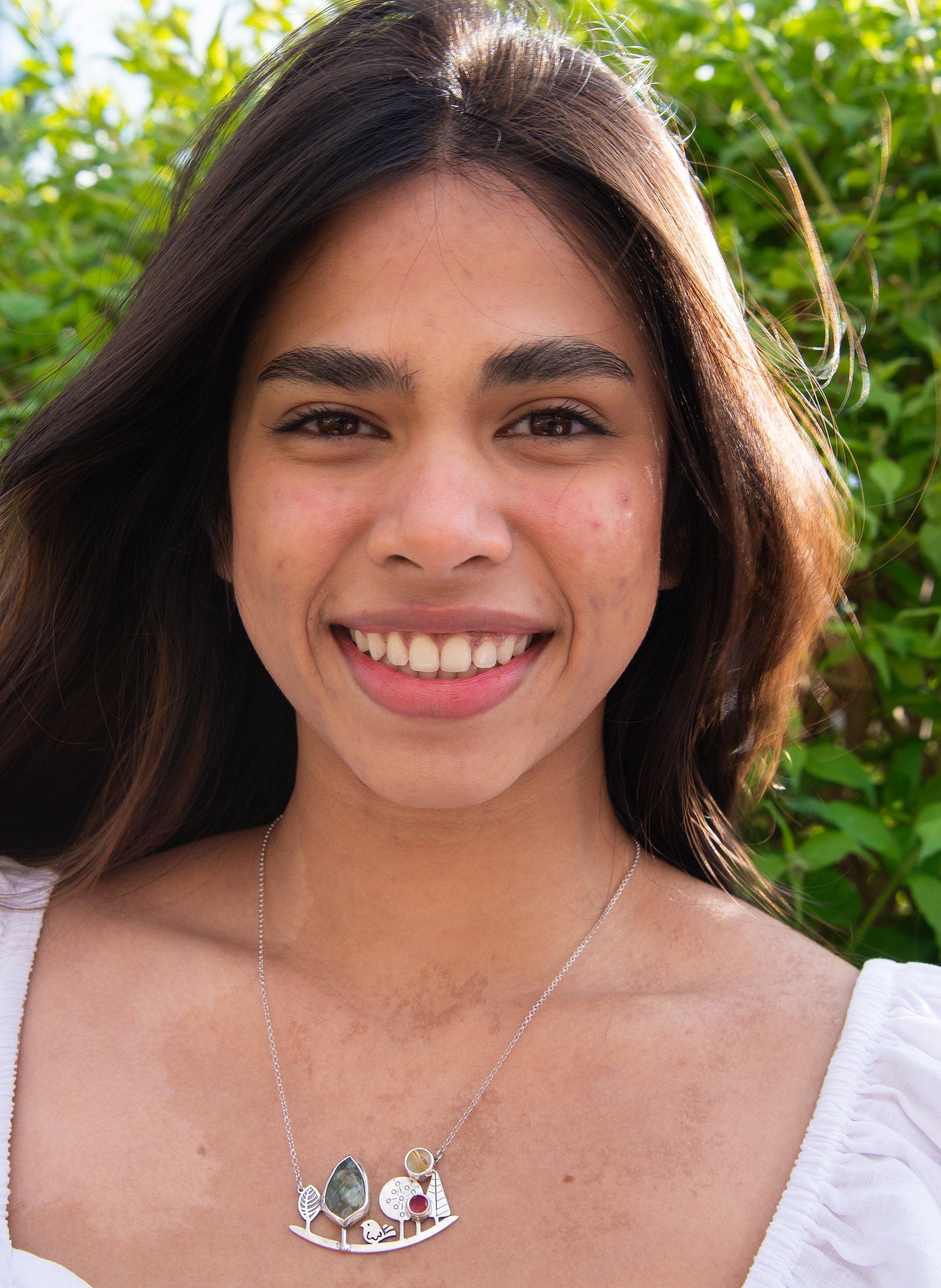 Close-up image featuring a woman wearing a Landscape Silver Necklace against a vibrant outdoor background.