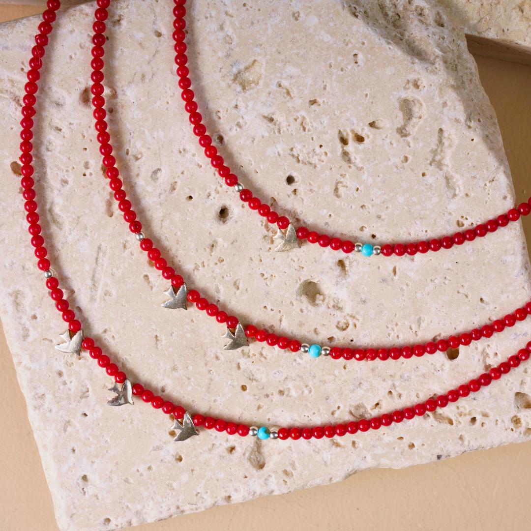 Minimal coral gemstone necklace adorned with silver bird pendants, displayed on a textured stone surface.