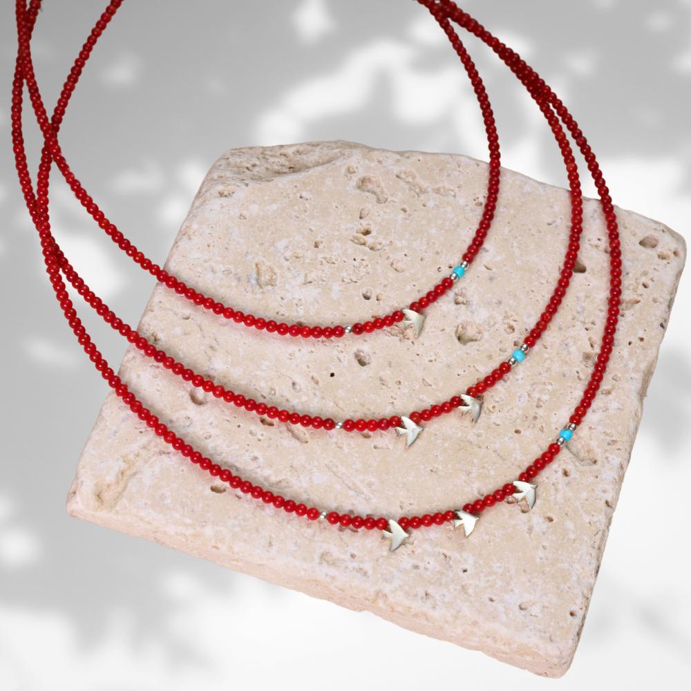 Minimal coral gemstone necklace adorned with silver bird pendants, displayed artistically on a textured stone surface.