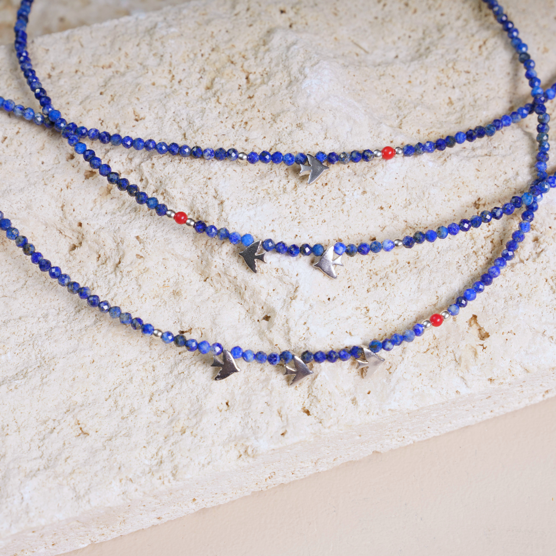 Minimalist lapis lazuli gemstone necklace featuring silver bird-shaped pendants set gracefully on a beige textured surface.