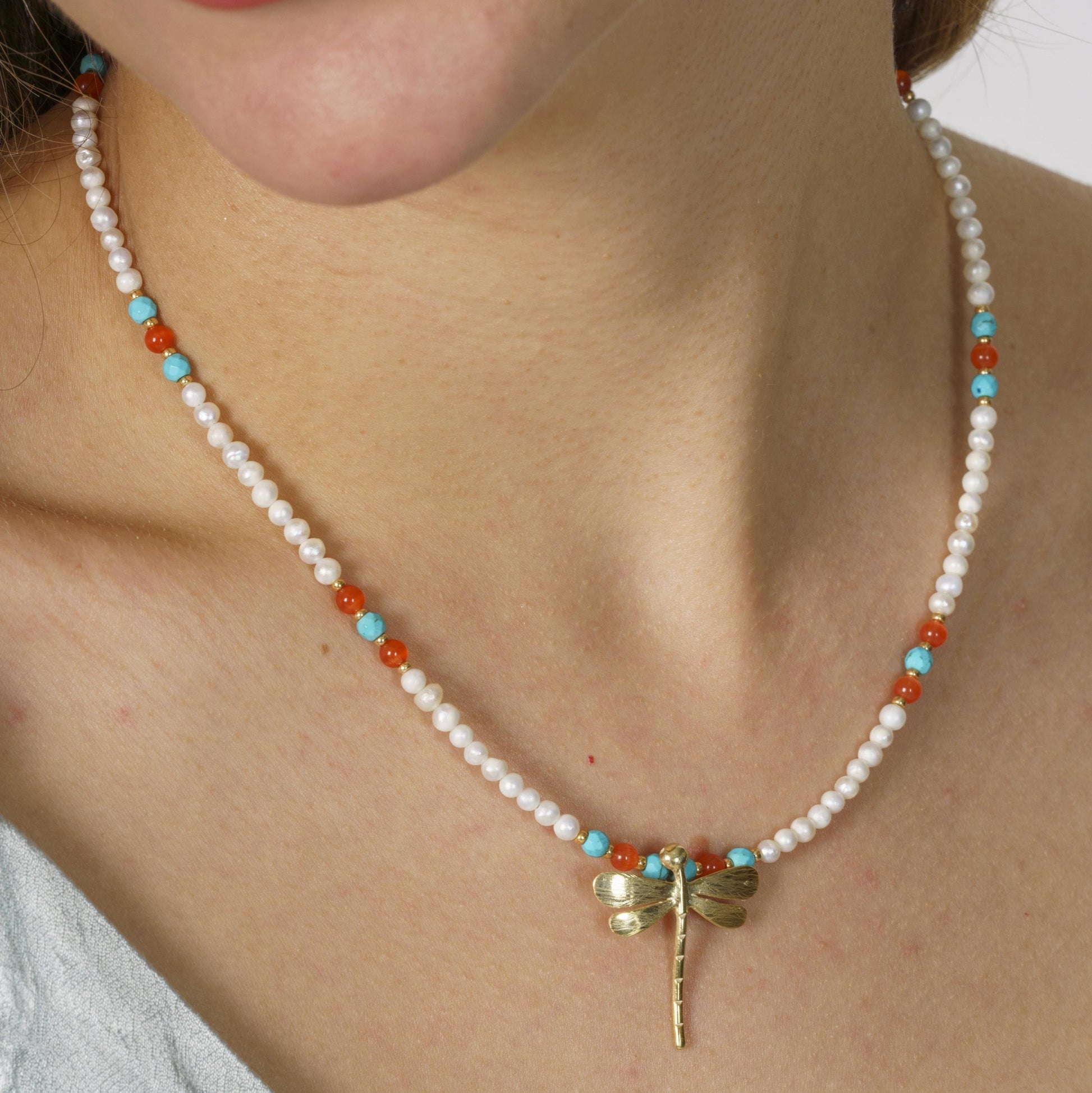 A delicate pearl and gemstone necklace featuring a silver dragonfly pendant, elegantly worn by a model, showcasing its beauty.