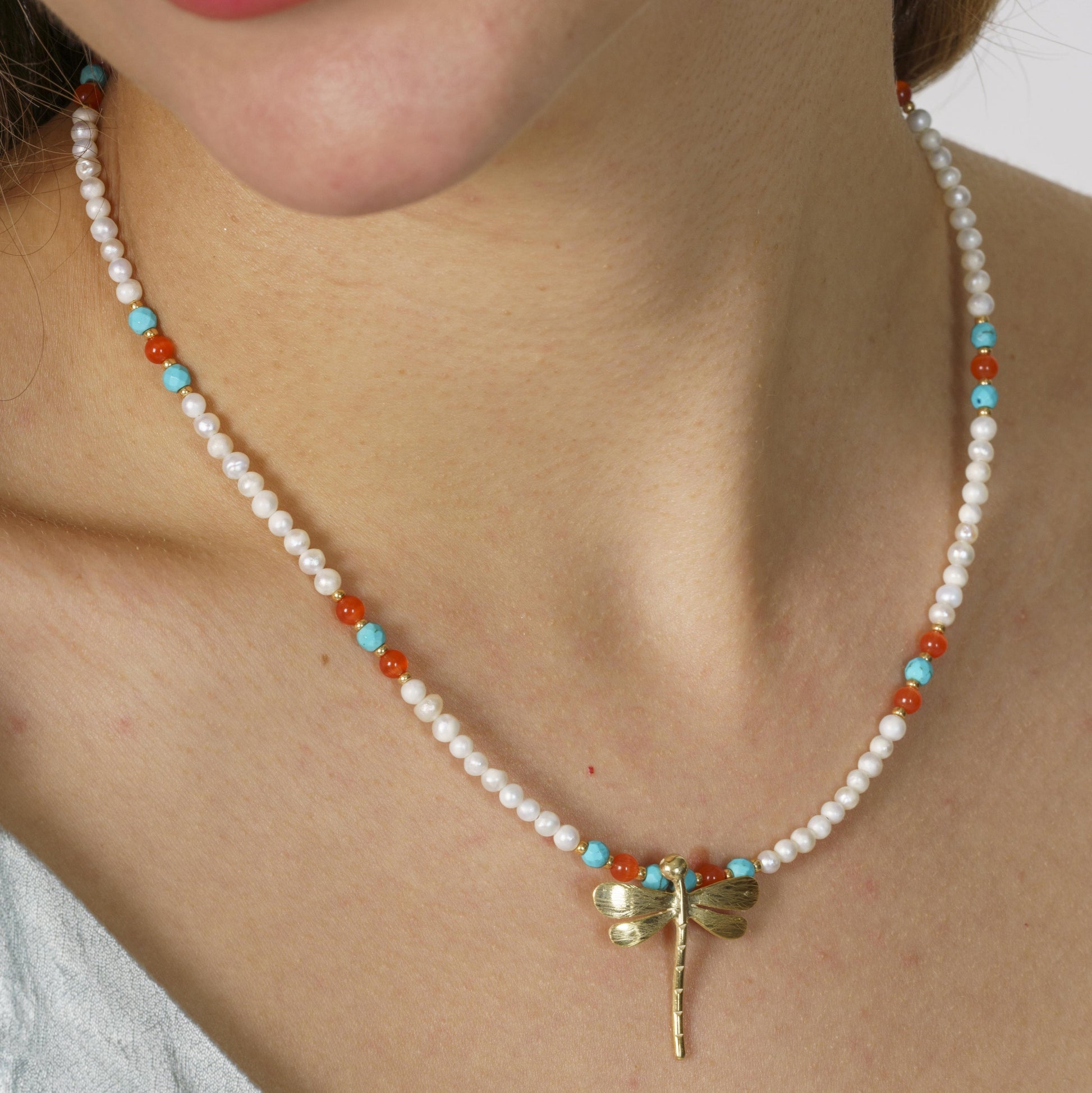 Elegant pearl and gemstone necklace featuring a silver dragonfly pendant, showcased on a model's neck