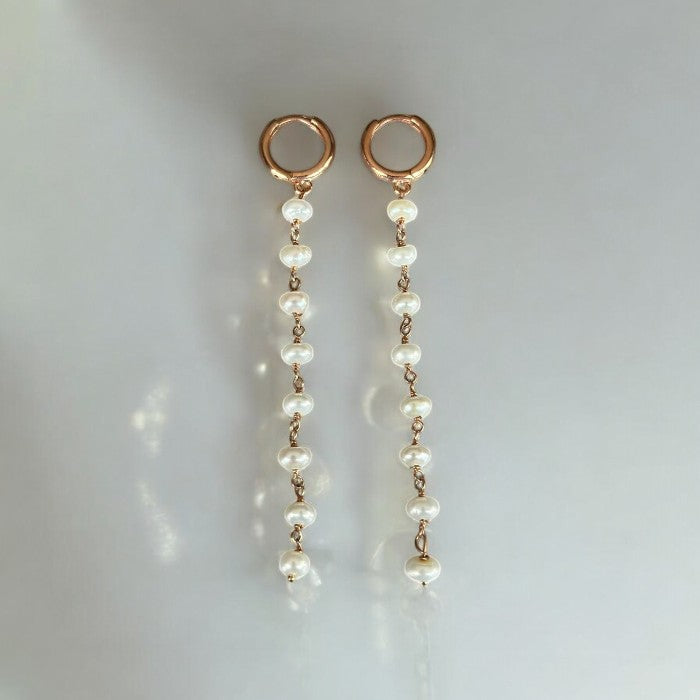 Elegant pearl long chain drop earrings with gold accents displayed on a soft grey background gleaming under ambient light.
