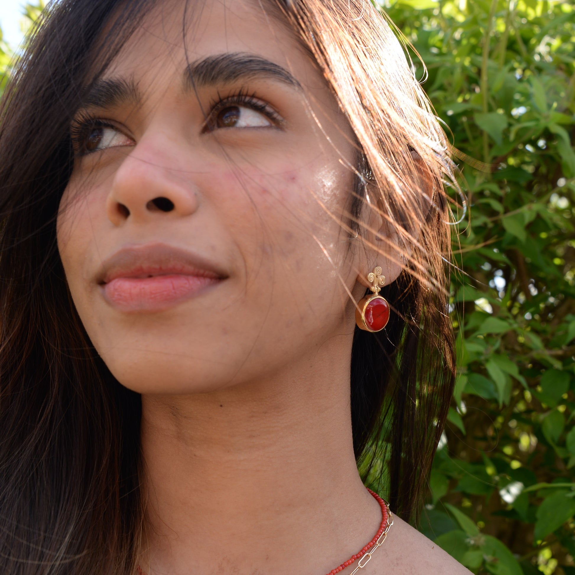 A model showcasing Rho Natural Coral Gemstone Earrings, set against lush greenery, emitting a radiant and elegant aura.