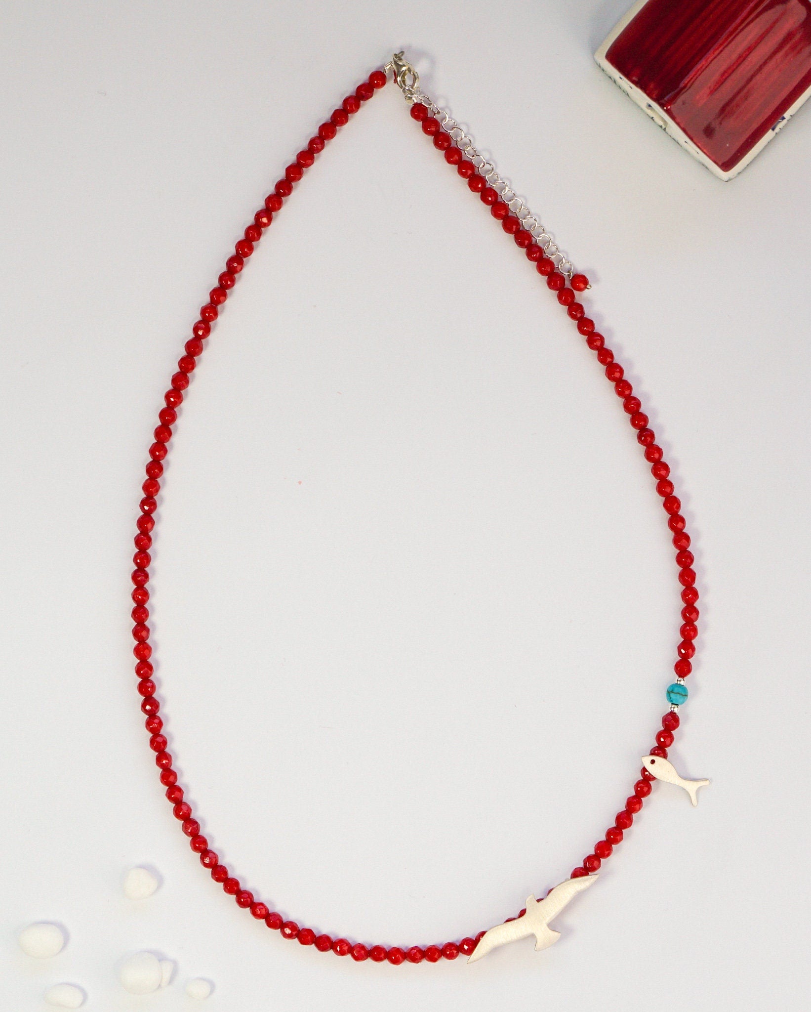 Red coral and silver necklace featuring seagull and fish charms, laid against a light background for a detailed view.