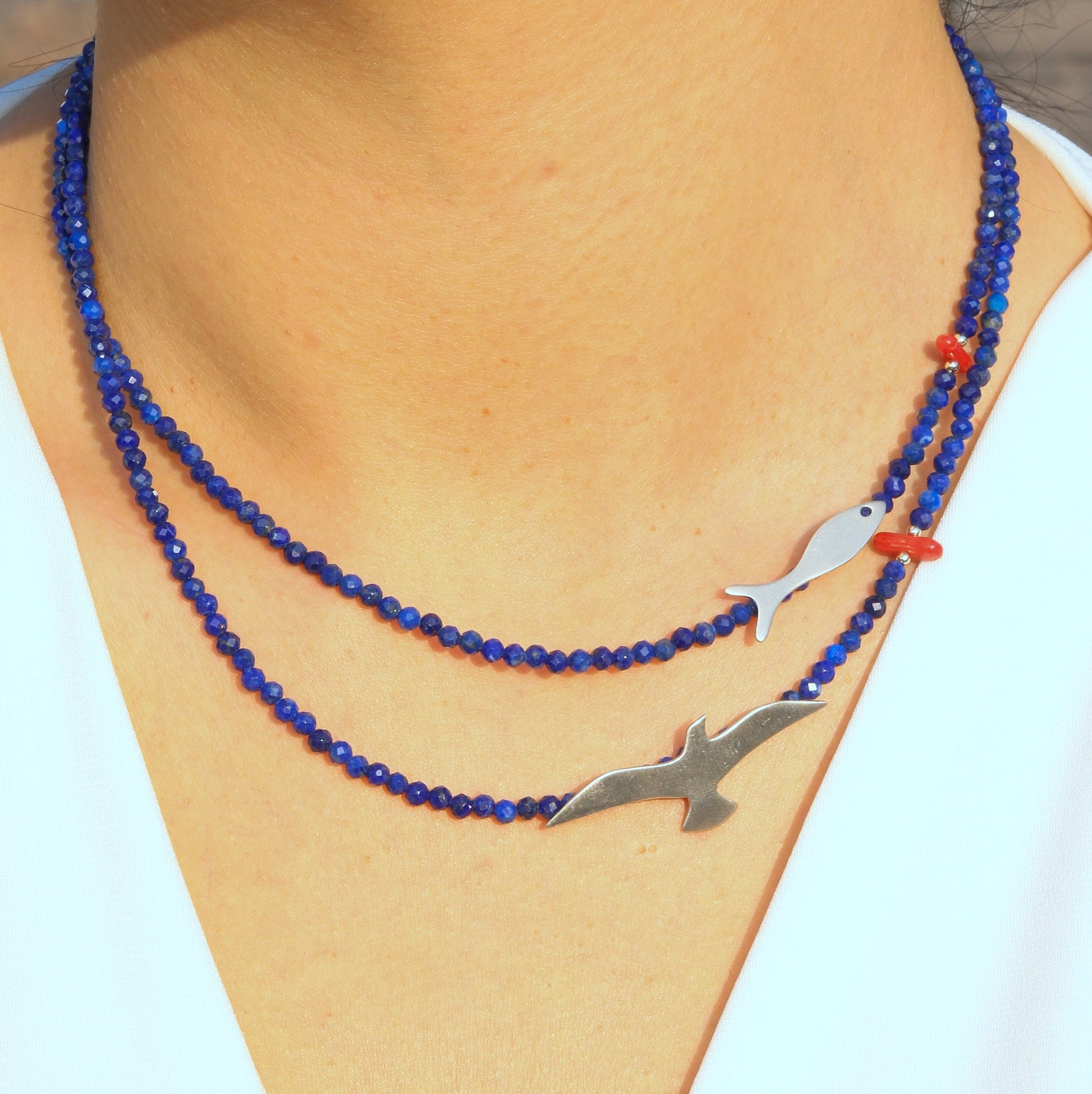 A detailed close-up of the Seagull & Fish necklace featuring lapis beads and silver charms in a coastal-inspired design.
