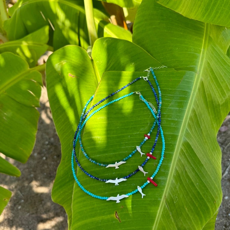 Seagull and Fish Lapis and Silver Necklace displayed on a green leaf in natural light, showcasing its intricate design.