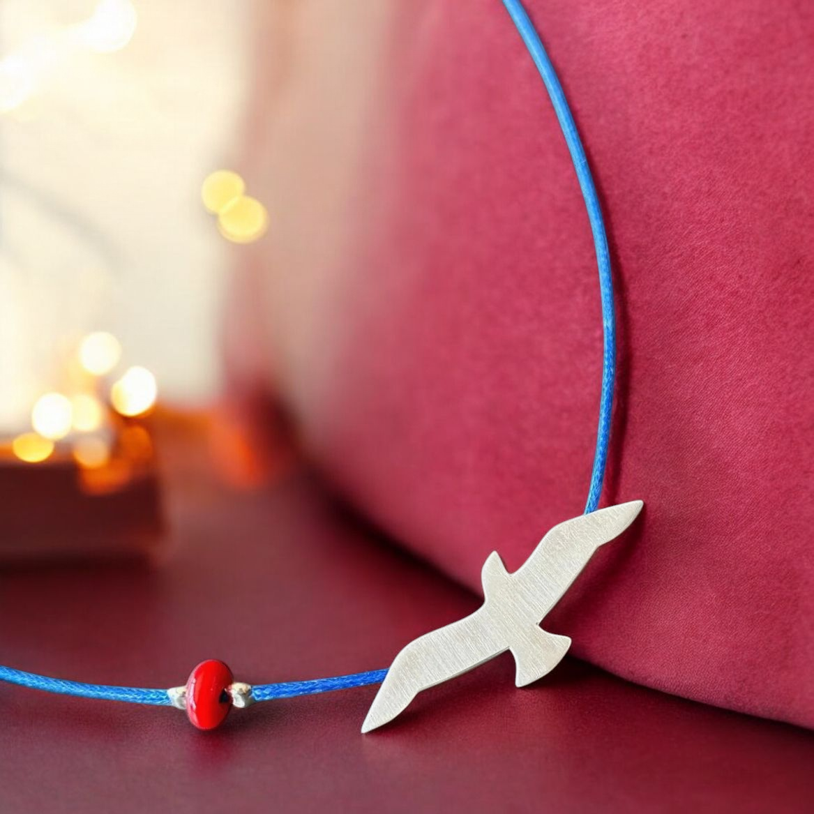 Elegant silver seagull pendant on blue cord necklace with red bead, perfect for a nautical-inspired style.
