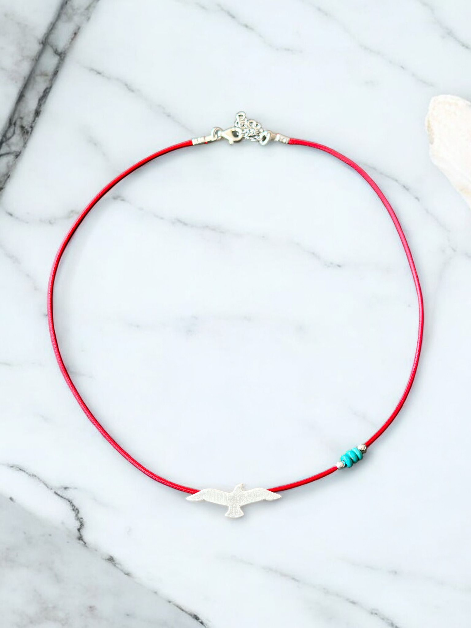 Elegant silver seagull pendant on red cord necklace, laid out on a marble surface.