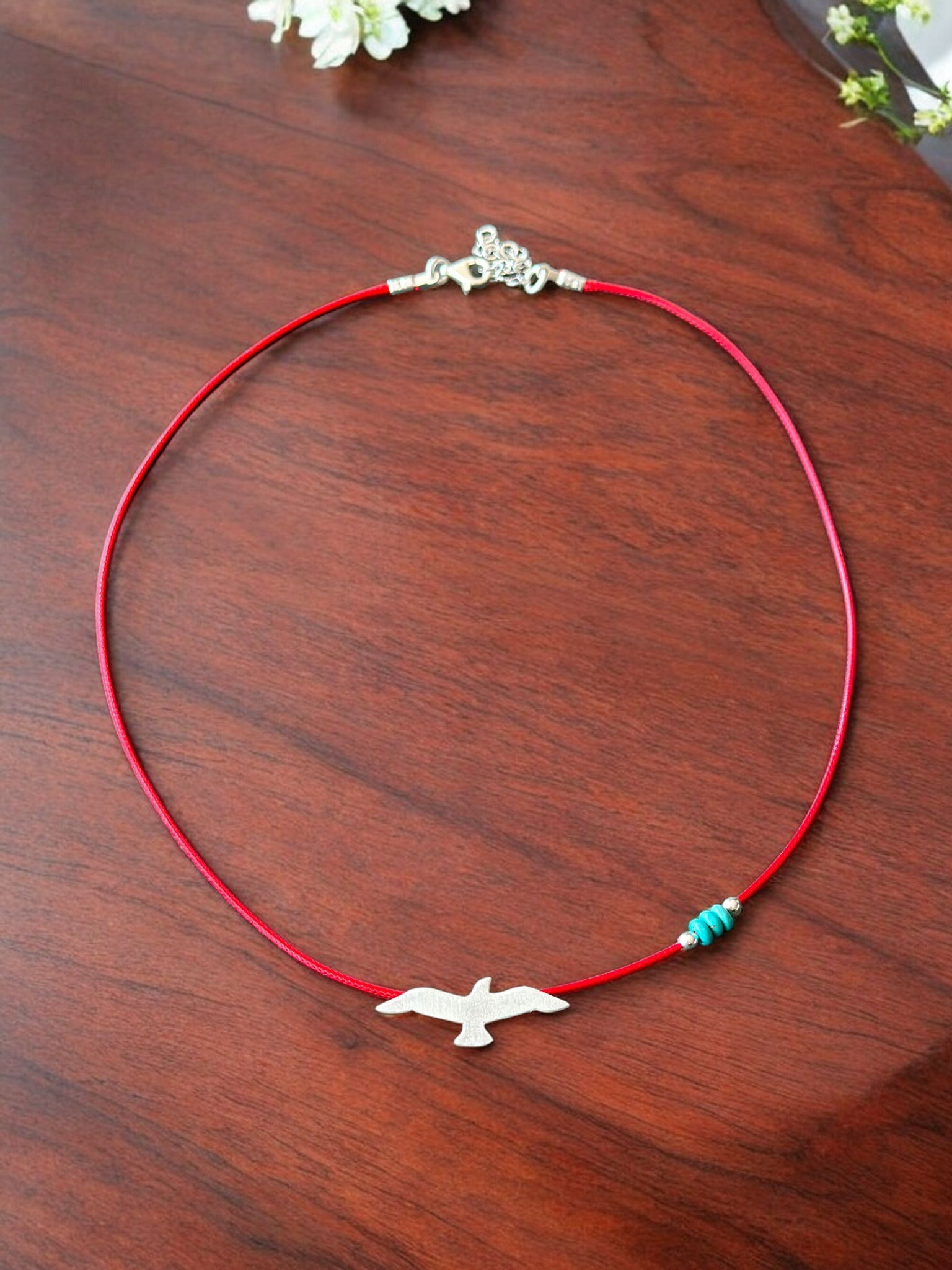 Silver seagull pendant on a vibrant red cord necklace with turquoise beads, displayed on a wooden surface.