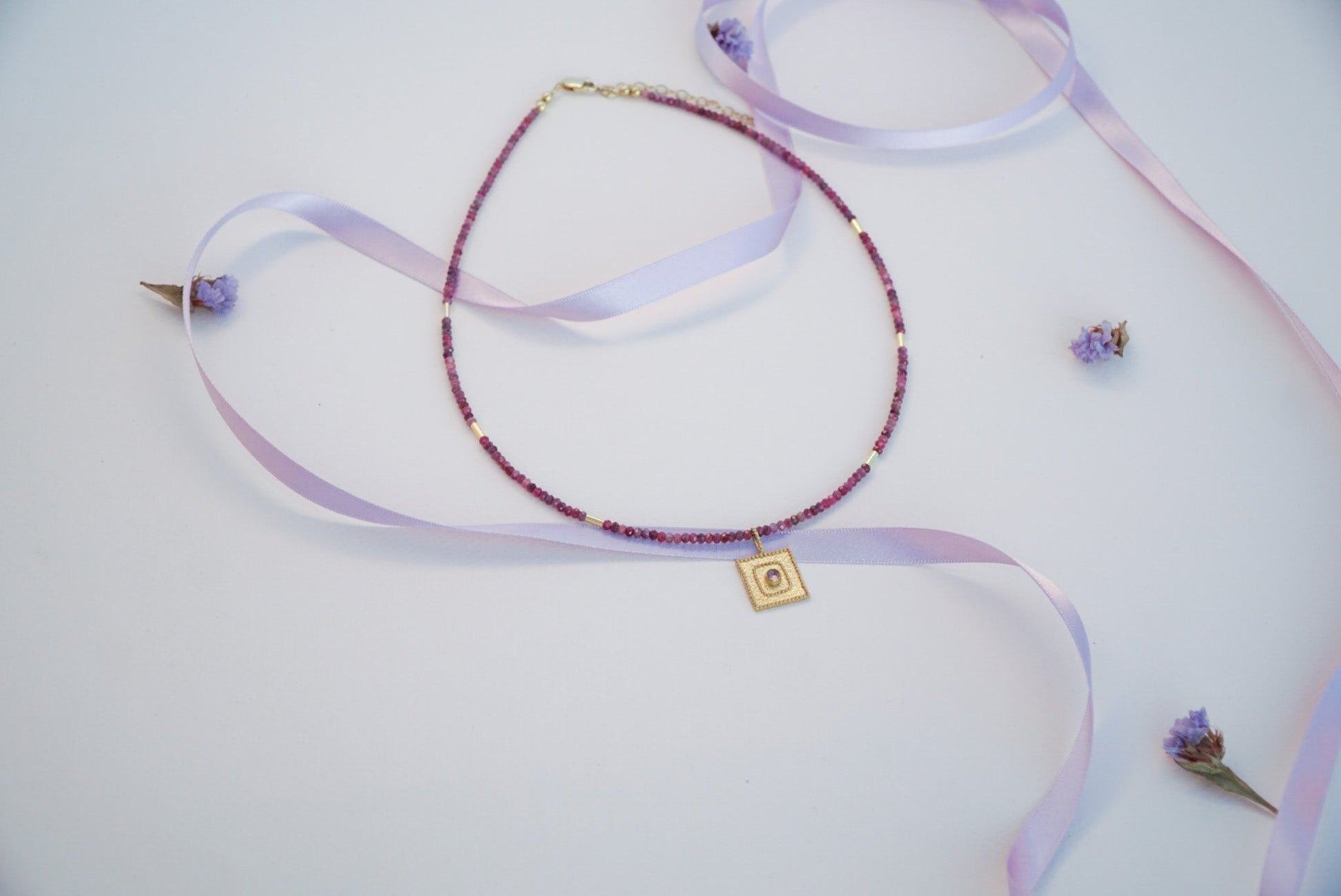 Tourmaline Gemstone Necklace with 14K Gold Plated 925 Sterling Silver Pendant on a light background with lavender ribbon and flowers