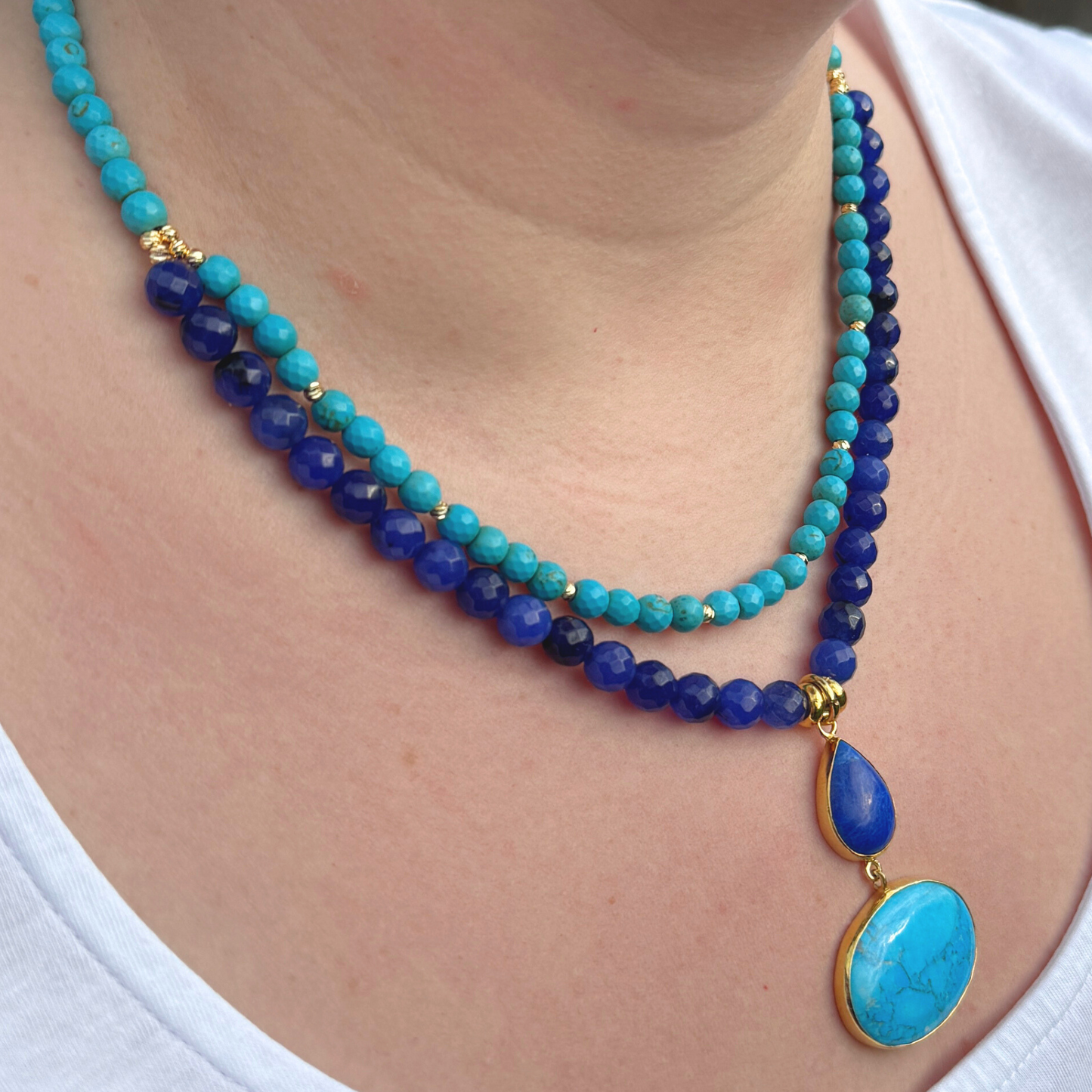A stylish turquoise and lapis lazuli gemstone necklace featuring blue beads and a pendant, shown worn by a model on a white top.